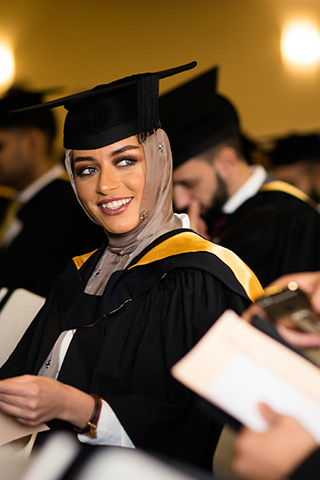 Female student in graduation gown in hall full of other students in graduation gowns