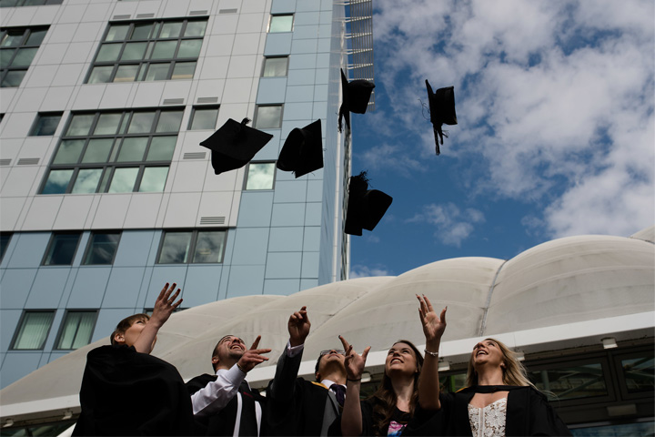 A group of graduates in front of the Richmond Building throwing their graduation caps into the air