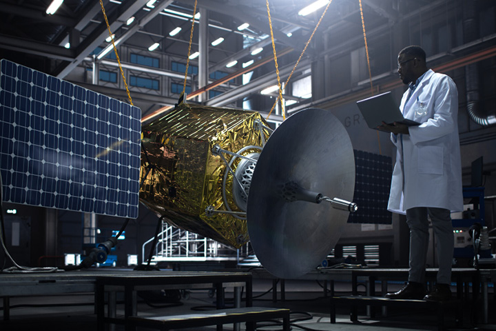 A person in a labcoat and clipboard inspecting a satellite.