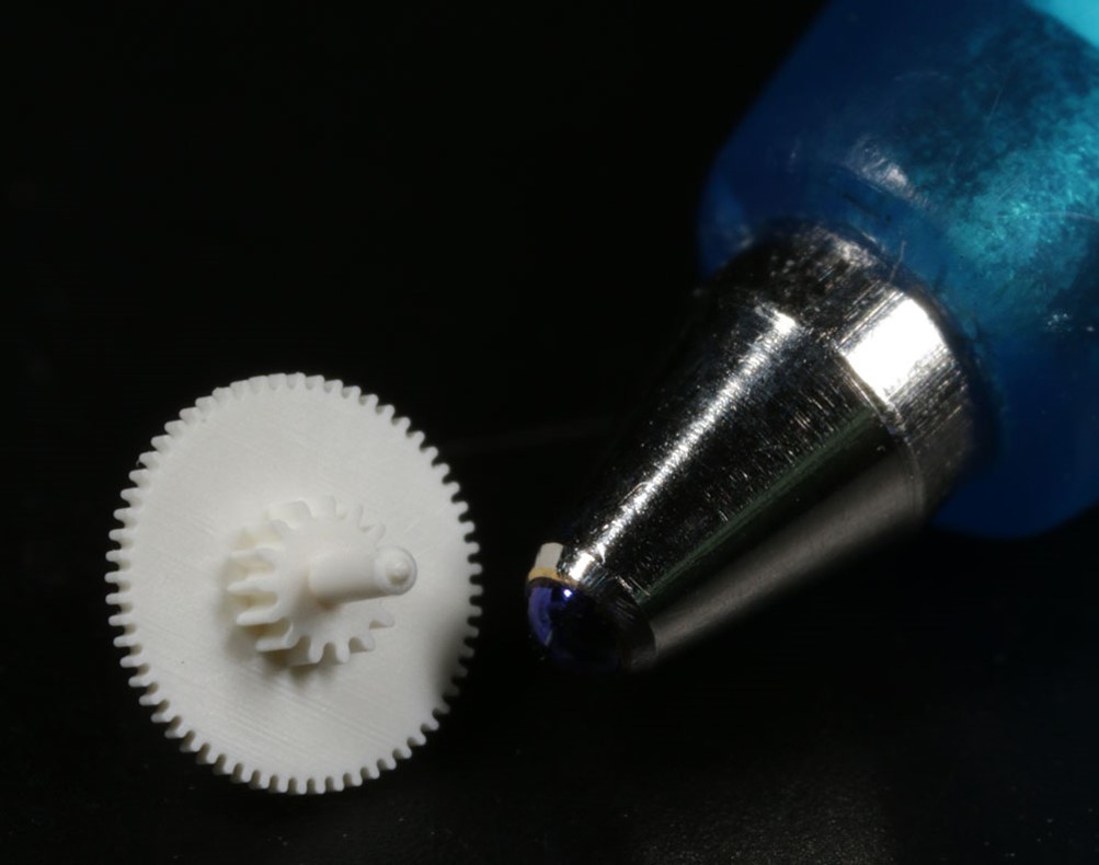 Close up of a gear and the nib of a ball-point pen to emphasize the smallerness of the gear,