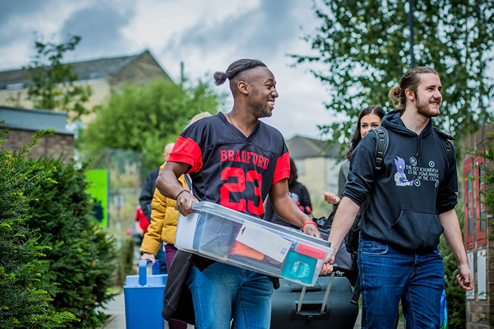 Student holding a box and student pulling a travel case, ready to move into our on-campus accommodation.