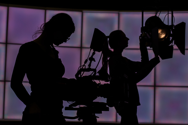Silhouettes of people working with TV and film equipment.