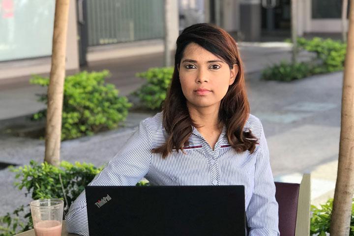 MBA student Farzanah Maudarbaccus sitting at a table using a laptop