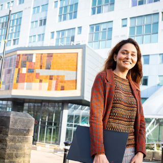 A postgraduate student standing in front of Richmond Building on the University of Bradford campus.