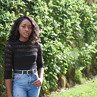 Poshia Boateng, stood outside in front of a hedge.