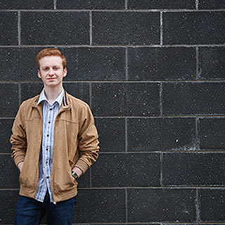 Connor Harrison, BSc (Hons) Marketing stood in front of a wall.