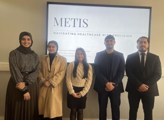 Five students dressed smartly stand up in front of projector screen with Metis written on it Five students dressed smartly stand up in front of projector screen with Metis written on it