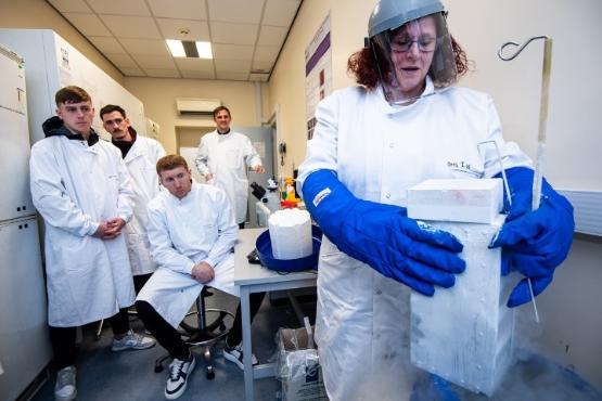 Four people in the background wearing white lab coats look on as a scientist at the front conducts an experiement Four people in the background wearing white lab coats look on as a scientist at the front conducts an experiement