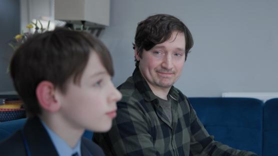 An adult looking over proudly at a young boy as they sit on a sofa together An adult looking over proudly at a young boy as they sit on a sofa together