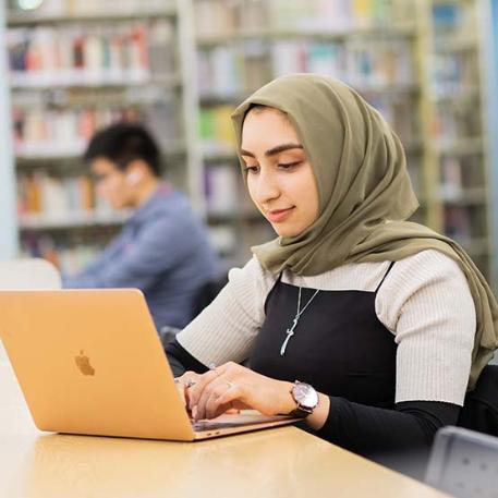 A student typing on their laptop in the library.