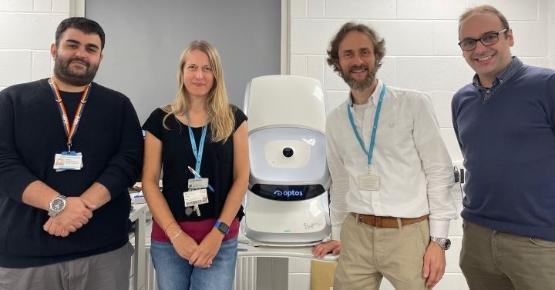 Two university staff members stand either side of a large white machine used for optometry Two university staff members stand either side of a large white machine used for optometry