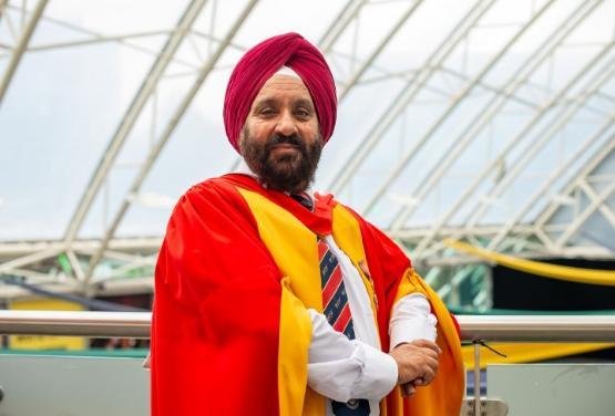 Honorary graduate dressed in gown stands for photograph Honorary graduate dressed in gown stands for photograph