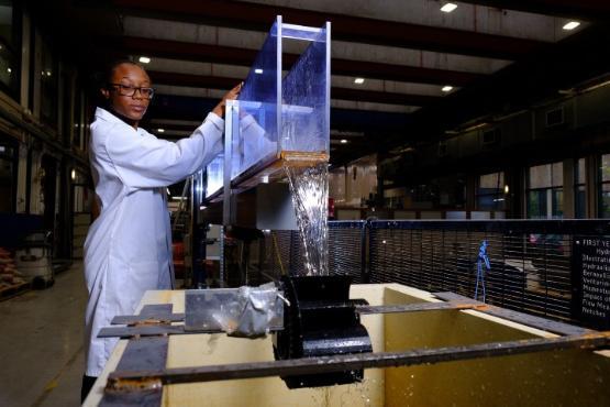 A university student in a white coat and protective glasses stands up and carries out an experiment with water dripping off the end of a plastic box A university student in a white coat and protective glasses stands up and carries out an experiment with water dripping off the end of a plastic box
