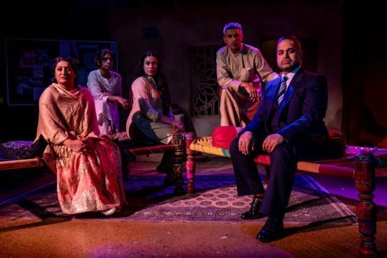 The cast of a play on stage in their costumes sat down facing a camera for a group photograph The cast of a play on stage in their costumes sat down facing a camera for a group photograph