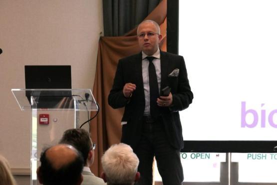 A person holding a mobile phone stands talking on a stage at a conference A person holding a mobile phone stands talking on a stage at a conference