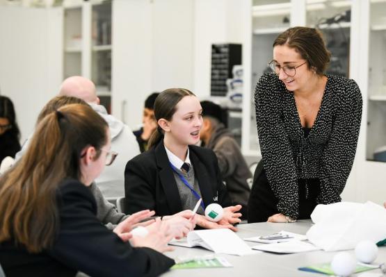 An adult stood up talking to two school students who are sat down An adult stood up talking to two school students who are sat down