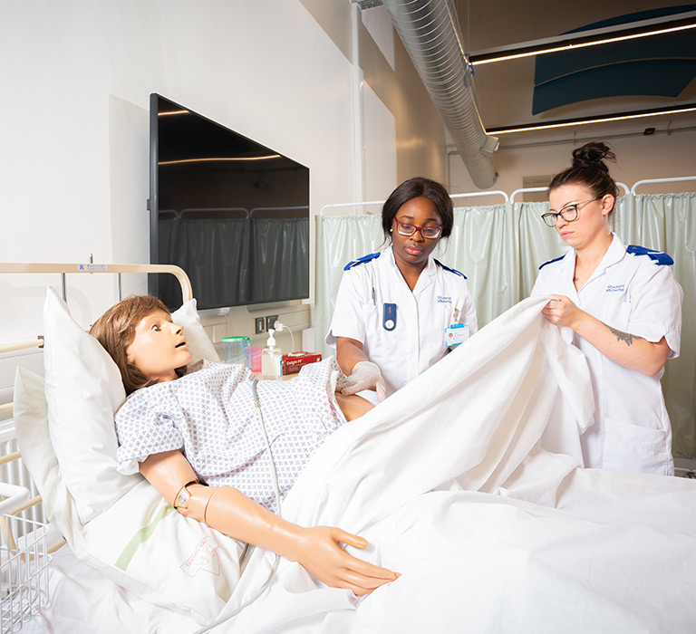 Two student midwives practicing on SimDoll.