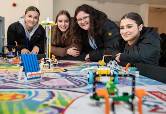 Four students stood around a table with a number of Lego models on it Four students stood around a table with a number of Lego models on it