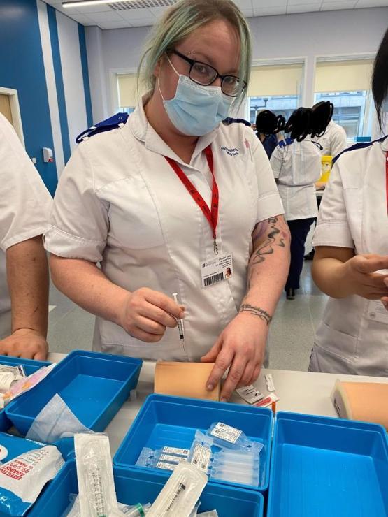 A university student in a nursing uniform wearing a face mask holds a syringe during a practical medical lesson A university student in a nursing uniform wearing a face mask holds a syringe during a practical medical lesson