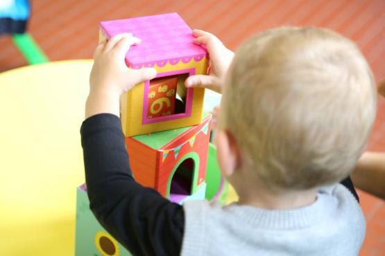 A toddler makes a tower out of small plastic toys in front of them