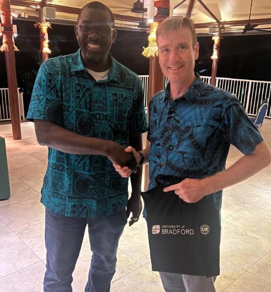 Two people stand next to each other and shake hands while one holds a University of Bradford tote bag Two people stand next to each other and shake hands while one holds a University of Bradford tote bag