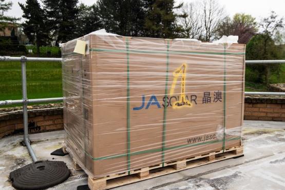 A large wooden pallet covered in see-through film wrap which is filled with solar panels A large wooden pallet covered in see-through film wrap which is filled with solar panels