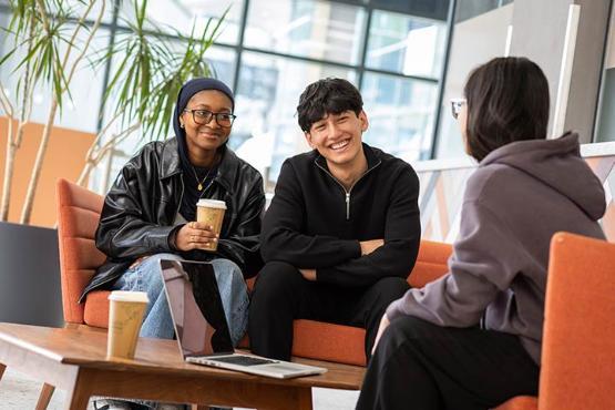 Three students sitting on red chairs and chatting.