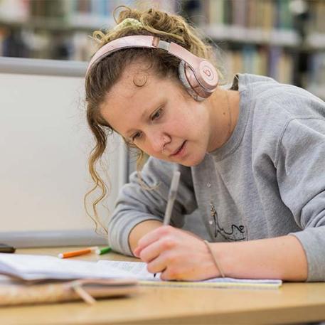 A student writing in a notepad with headphones on.