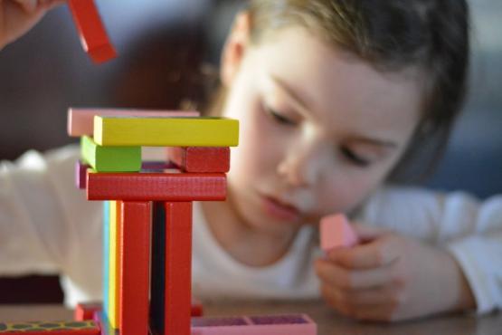 A toddler aged child looks on as they build a small tower made out of wooden blocks A toddler aged child looks on as they build a small tower made out of wooden blocks