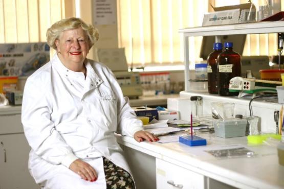 An academic wearing a white coat sitting down inside a laboratory An academic wearing a white coat sitting down inside a laboratory