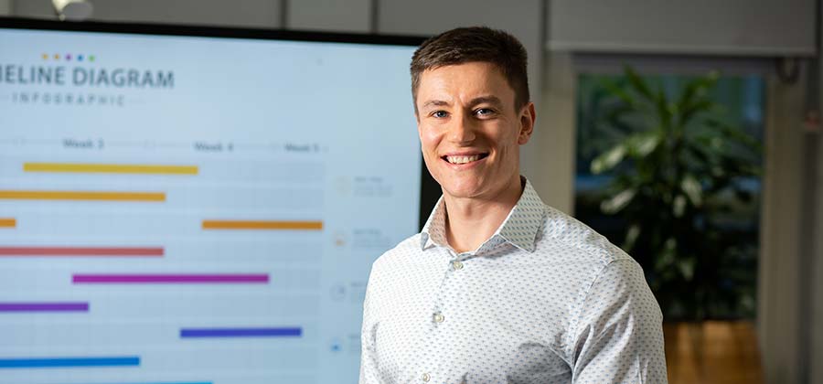 A student smiling at the camera whilst giving a presentation.