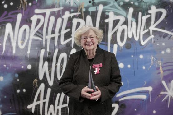 An academic holds an award stood in front of banner with large graffiti style lettering written on it An academic holds an award stood in front of banner with large graffiti style lettering written on it