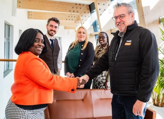 Three people stood up behind two other people at the front who are also stood up shaking hands with each other Three people stood up behind two other people at the front who are also stood up shaking hands with each other