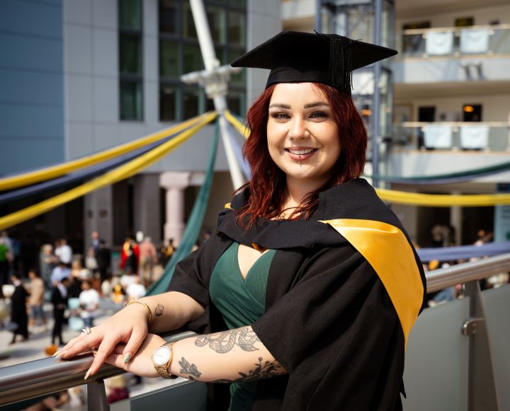 Student dressed in graduation gown poses for a photo