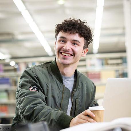 A student smiling with a coffee and their laptop.