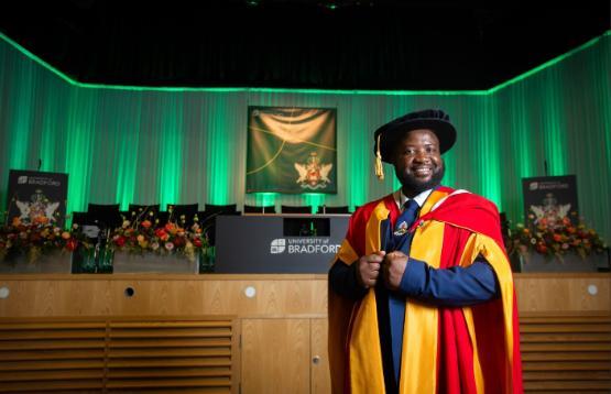 Elgidius Edgar Bwinabona Ichumbaki stands in gown and hat in front of stage at Graduation ceremony Elgidius Edgar Bwinabona Ichumbaki stands in gown and hat in front of stage at Graduation ceremony