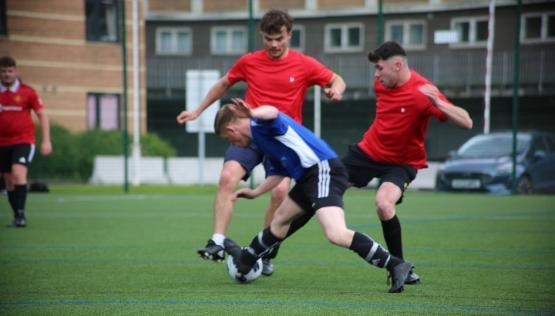 A football player in a blue shirt is falling onto the ground as two players in red shirts tackle them A football player in a blue shirt is falling onto the ground as two players in red shirts tackle them