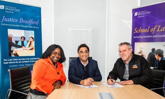 Three people sat behind a wooden desk in a room Three people sat behind a wooden desk in a room
