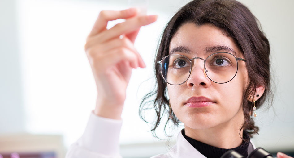 A student wearing a lab coat examining a sample.