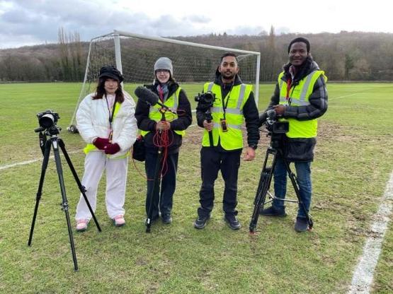 a group of four students in high-vis jackets standing on a grass football pitch a group of four students in high-vis jackets standing on a grass football pitch