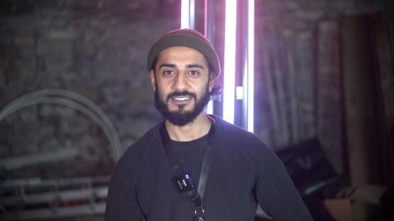 A person smiling wearing a beanie hat in front of a neon lighting strip A person smiling wearing a beanie hat in front of a neon lighting strip