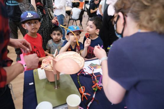 A group of four children stood behind a table look at a demonstration at a community day A group of four children stood behind a table look at a demonstration at a community day