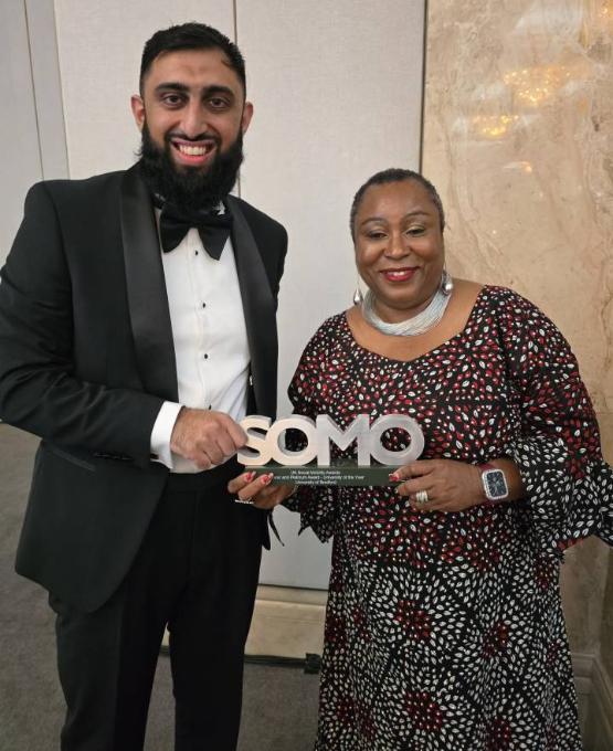 Two members of university staff in formal wear hold an award won at a ceremony Two members of university staff in formal wear hold an award won at a ceremony