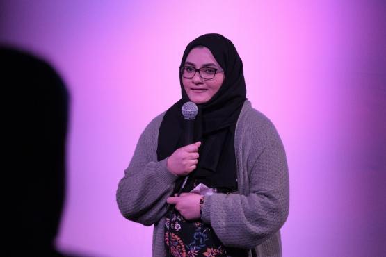 A person wearing a head dress holds a microphone and delivers a stand-up comedy routine A person wearing a head dress holds a microphone and delivers a stand-up comedy routine