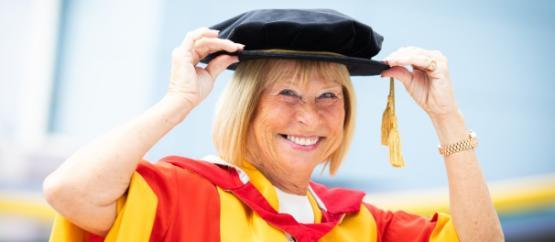Dame Irene Hays posing in her honorary graduation gown, touching her hat