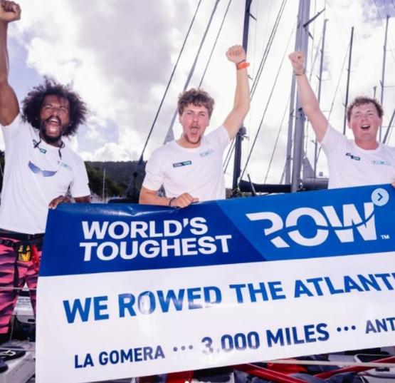 Three graduates stood next to each other on boat hold arms up to celebrate holding large sign in front of them Three graduates stood next to each other on boat hold arms up to celebrate holding large sign in front of them