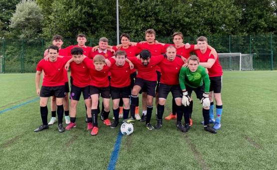 A large group of football players in kit with red shirts line up for a team group photograph on the pitch half standing and half of them crouching in front of them A large group of football players in kit with red shirts line up for a team group photograph on the pitch half standing and half of them crouching in front of them