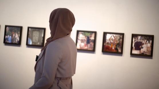 A person with their back to the camera looks over at a series of photographs hanging on a wall at an exhibition A person with their back to the camera looks over at a series of photographs hanging on a wall at an exhibition