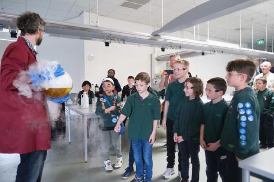 A scientist shows off a large glass container which is bubbling over to a group of people in a university room A scientist shows off a large glass container which is bubbling over to a group of people in a university room