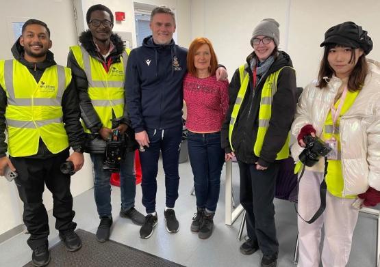 A group of students and staff stand up for photo with football manager wearing a tracksuit A group of students and staff stand up for photo with football manager wearing a tracksuit